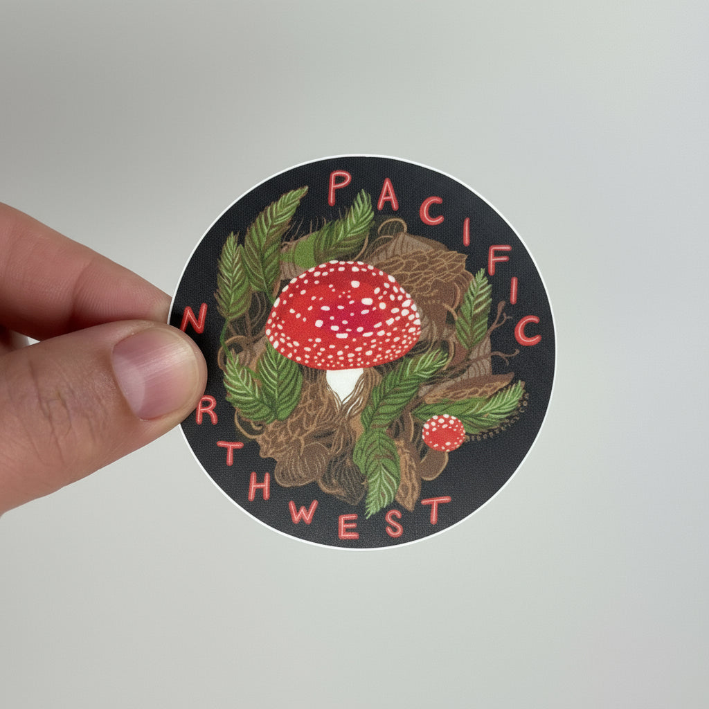 Sticker with a mushroom design and 'Pacific Northwest' text held by a hand on a light gray background