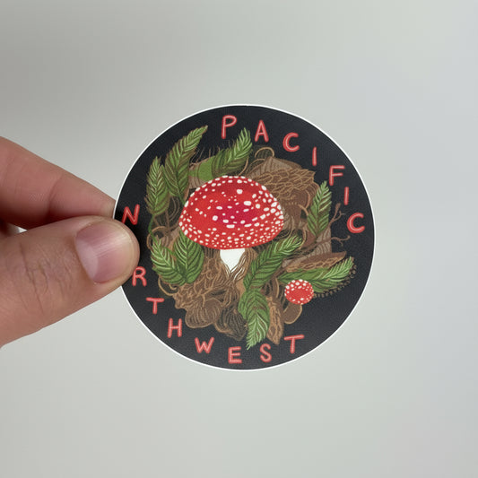 Sticker with a mushroom design and 'Pacific Northwest' text held by a hand on a light gray background